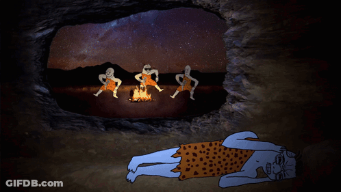 A Caveman Is Laying On The Ground In Front Of A Fire With Three Other Cavemen GIF