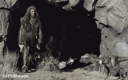 A Caveman Is Standing In Front Of A Cave GIF
