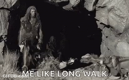 A Caveman Is Walking Through A Cave With A Dog . GIF