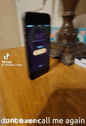 A Cell Phone Is Sitting On A Wooden Table Next To A Lamp And A Sign That Says Do N't Ever Call Me Again GIF