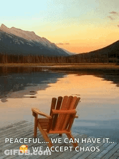A Chair Sits On A Dock Overlooking A Lake With Mountains In The Background . GIF