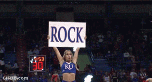 A Cheerleader Holds Up A Sign That Reads Rock GIF