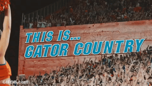 A Cheerleader In Front Of A Sign That Says This Is Gator Country GIF