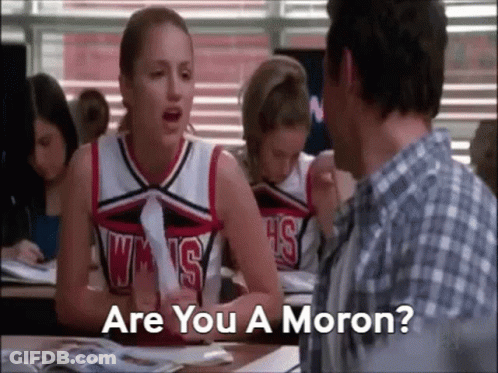A Cheerleader Is Sitting At A Desk Talking To A Man In A Classroom While A Man Looks On . GIF