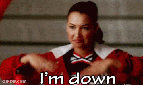 A Cheerleader Is Sitting At A Table With Her Hands Folded And The Words `` I 'M Down '' Written Below Her . GIF