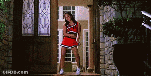 A Cheerleader Is Standing In Front Of A Door Wearing A Red Skirt . GIF
