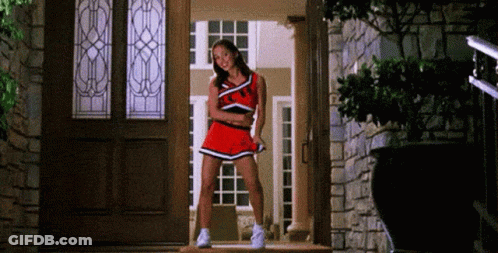 A Cheerleader Is Standing In Front Of A Door Wearing A Red Uniform . GIF