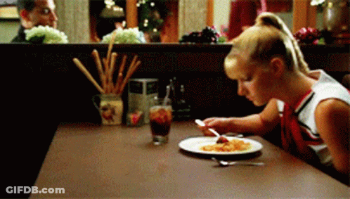 A Cheerleader Sits At A Table With A Plate Of Food On It GIF