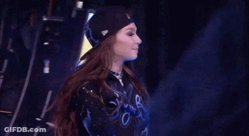 A Cheerleader Wearing A Black Hat And A Blue Shirt Is Standing On A Stage . GIF