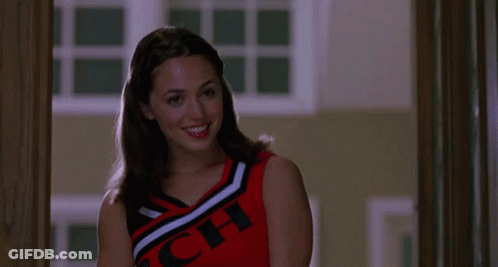 A Cheerleader Wearing A Red , Black And White Top With The Word Cheer On It Is Smiling . GIF