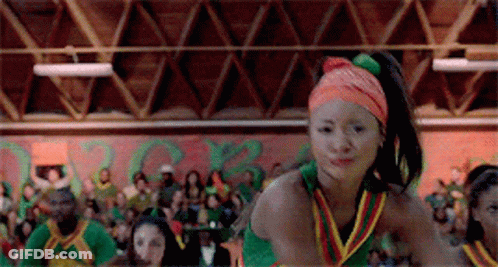 A Cheerleader Wearing An Orange Headband Is Dancing In Front Of A Crowd In A Gym . GIF
