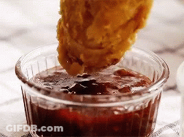 A Chicken Nugget Is Being Dipped Into A Small Bowl Of Sauce . GIF