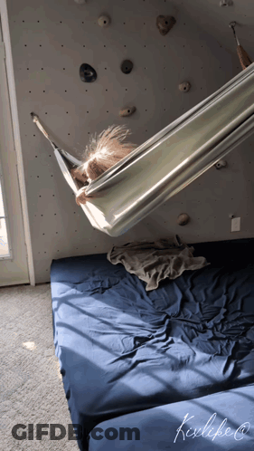 A Child Is Laying In A Hammock In Front Of A Wall With Rocks GIF