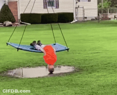 A Child Is Laying On A Blue Hammock In A Yard GIF
