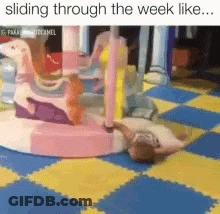 A Child Is Laying On The Floor In Front Of A Carousel . GIF