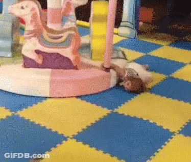 A Child Is Laying On The Floor In Front Of A Colorful Carousel GIF