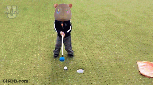 A Child Is Laying On The Grass With A Flag In Front Of A Golf Ball GIF