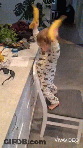 A Child Is Standing On A Chair And Holding A Banana In His Hands GIF