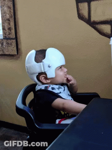 A Child Wearing A White Helmet Is Sitting In A Chair GIF
