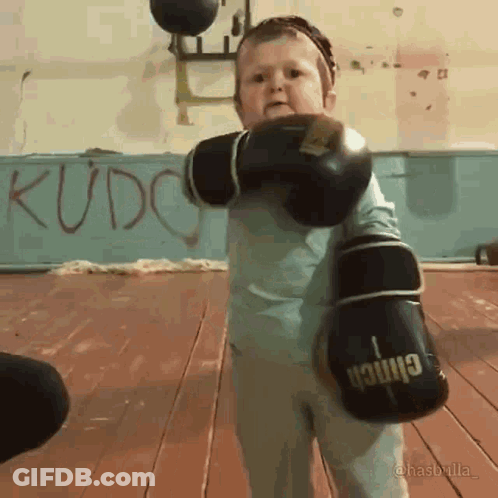 A Child Wearing Boxing Gloves With The Word Kudo On The Wall Behind Him GIF