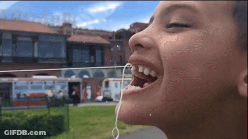 A Child With A String In His Mouth And A Building In The Background GIF