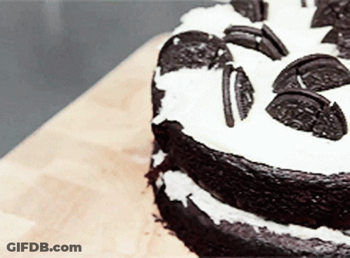 A Chocolate Cake With Oreos On Top Is On A Wooden Table GIF