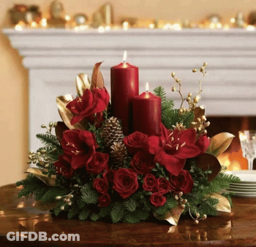 A Christmas Centerpiece With Red Candles And Red Flowers GIF