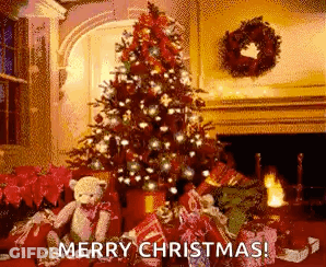 A Christmas Tree Is Sitting In Front Of A Fireplace In A Living Room Surrounded By Presents And A Teddy Bear . GIF