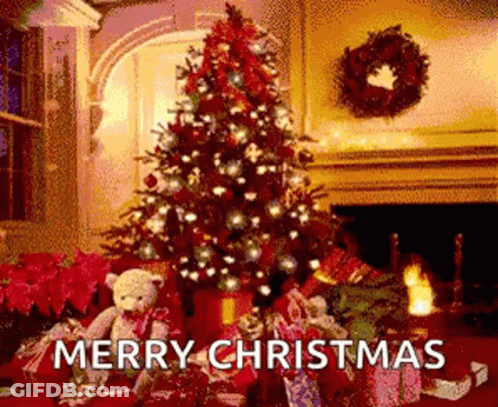 A Christmas Tree Is Sitting In Front Of A Fireplace In A Living Room With Gifts Underneath It . GIF