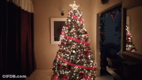 A Christmas Tree With A Star On Top Is Lit Up In A Room GIF