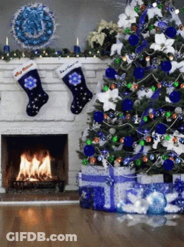 A Christmas Tree With Blue And Green Decorations And A Fireplace With Two Stockings Hanging From It GIF