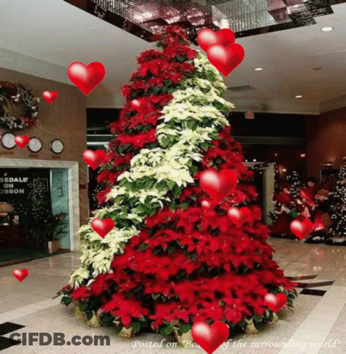 A Christmas Tree With Red And White Flowers And Hearts Surrounding It GIF