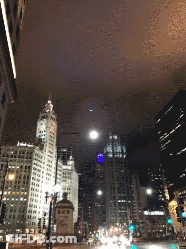 A City Street At Night With A Clock Tower And A Building That Says ' Bank Of America ' On It GIF