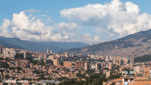 A Cityscape With Mountains In The Background And A Blue Sky GIF