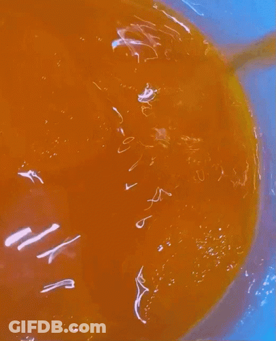 A Close Up Of A Bowl Of Orange Liquid With A Yellow Spoon In It GIF