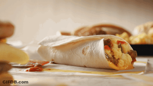 A Close Up Of A Burrito On A Table With Chips GIF