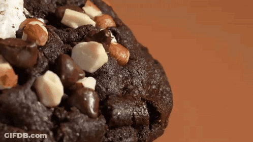 A Close Up Of A Chocolate Cookie With White Chocolate Chips And Nuts GIF