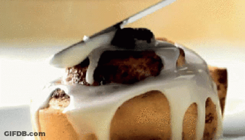 A Close Up Of A Cinnamon Roll With White Frosting On It GIF