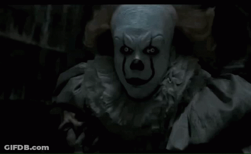 A Close Up Of A Clown In A Dark Room Looking At The Camera GIF