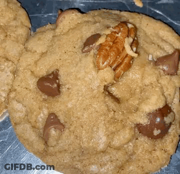 A Close Up Of A Cookie With Chocolate Chips And Pecans On It GIF