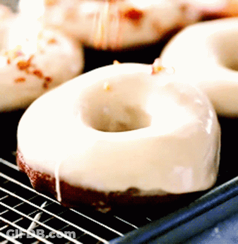 A Close Up Of A Donut With White Frosting On A Cooling Rack GIF