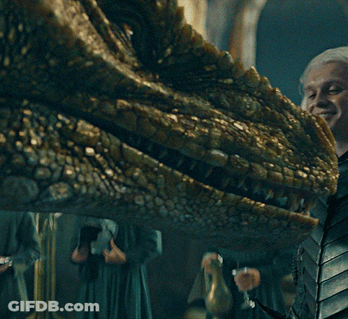 A Close Up Of A Dragon 'S Head With A Woman Holding A Glass Of Wine GIF