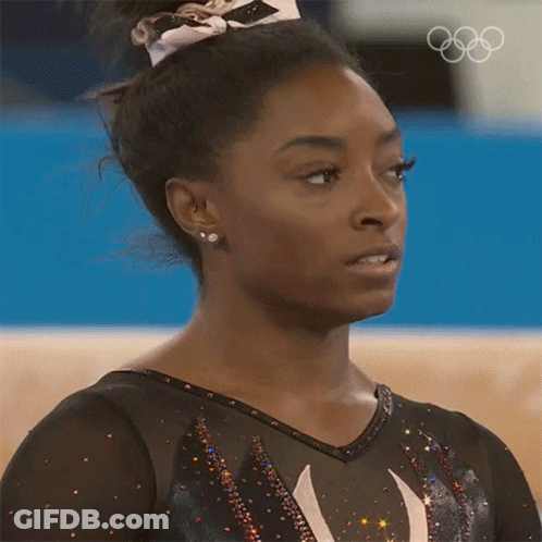 A Close Up Of A Female Gymnast 'S Face With The Olympic Rings Behind Her GIF