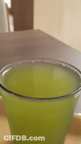 A Close Up Of A Glass Of Green Liquid On A Table . GIF