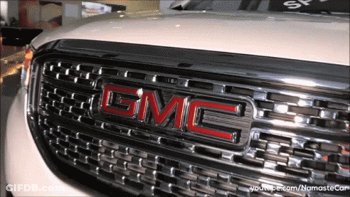 A Close Up Of A Gmc Logo On The Front Of A White Car GIF