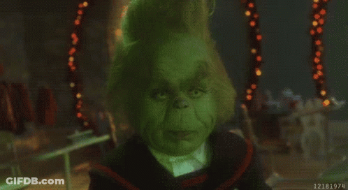 A Close Up Of A Grinch 'S Face In A Dark Room With Christmas Lights In The Background . GIF