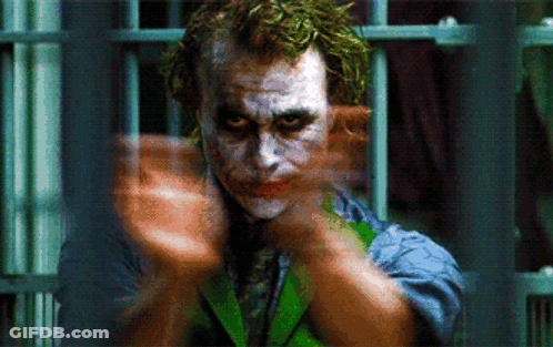 A Close Up Of A Joker Behind Bars With His Hands Outstretched GIF