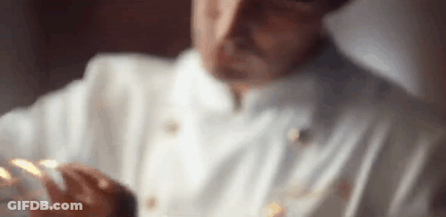 A Close Up Of A Man In A Chef 'S Uniform Holding A Piece Of Food . GIF