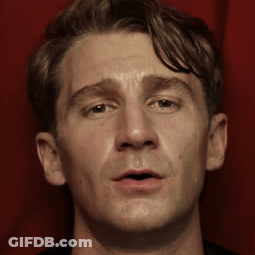 A Close Up Of A Man 'S Face Against A Red Curtain GIF