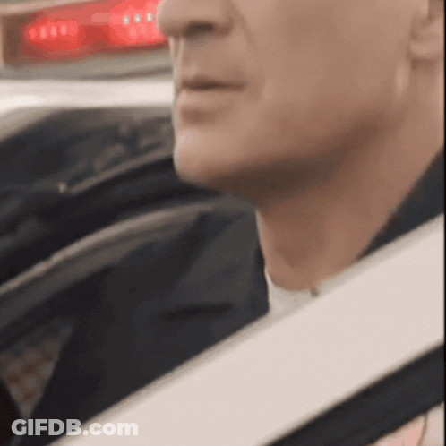 A Close Up Of A Man 'S Face In A Car With A Red Light Behind Him GIF